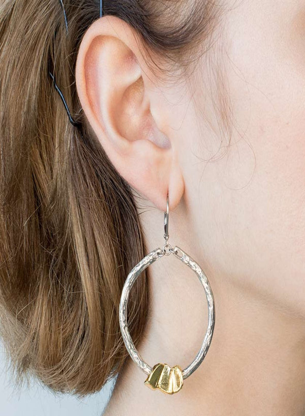 Portofino Earring By Anne Marie Chagnon features an organically textured silver pewter hoop with a single gold bead at the bottom of the hoop